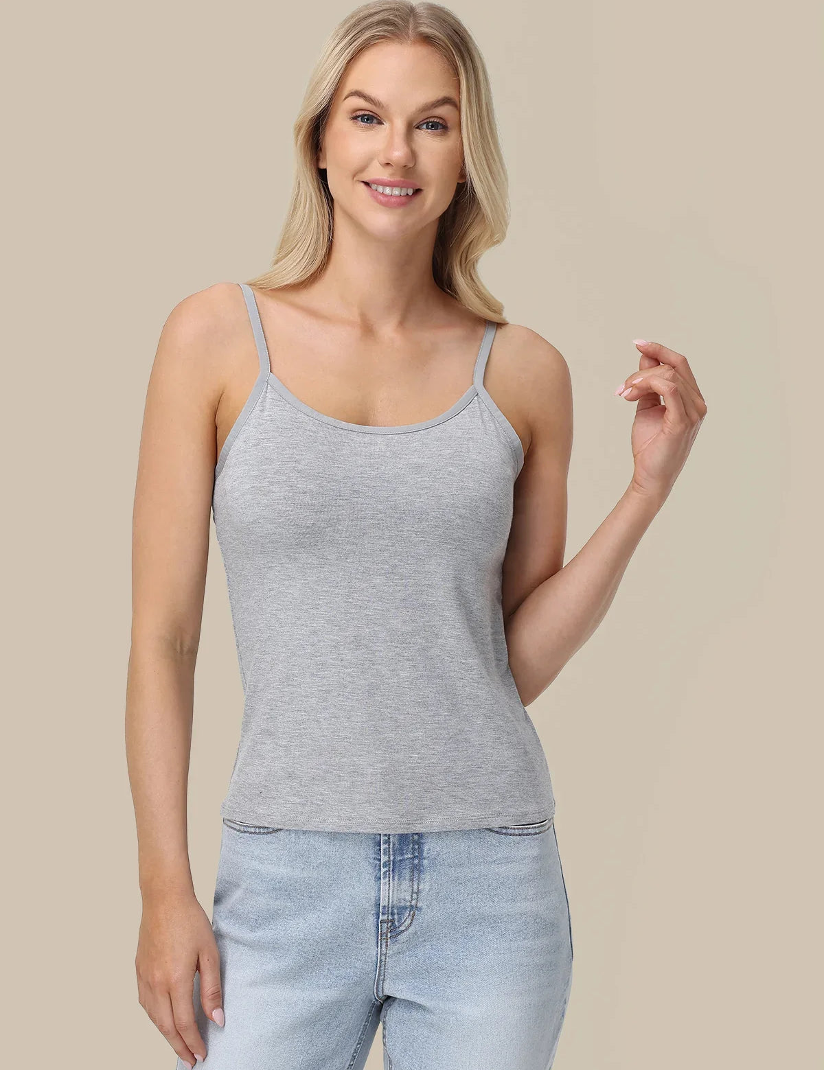 A woman modeling a light gray heather sleeveless camisole tank top with thin straps, paired with light-wash blue jeans, against a solid beige background.