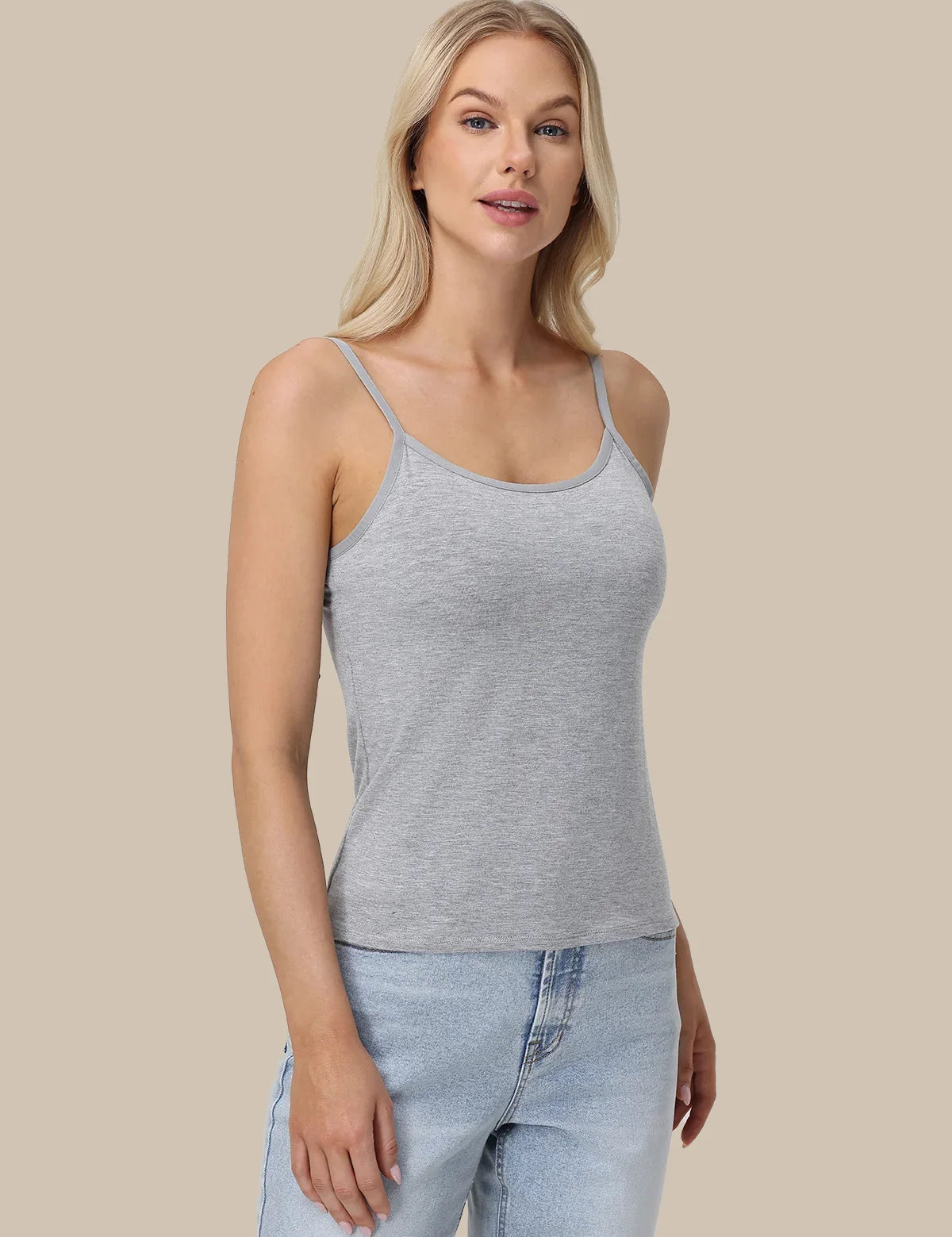 A blonde woman modeling a light gray heathered spaghetti-strap tank top with light-wash blue jeans, set against a solid beige studio background.