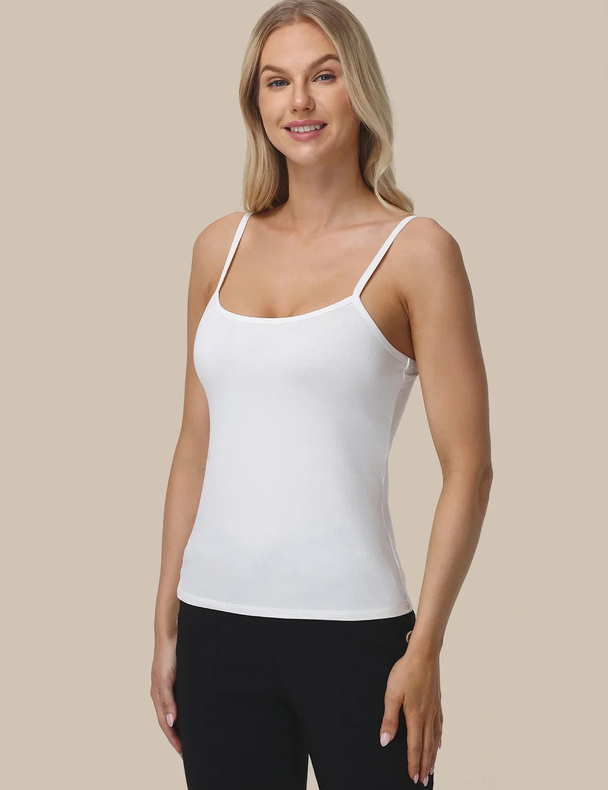 A woman modeling a white spaghetti-strap tank top against a solid beige background.