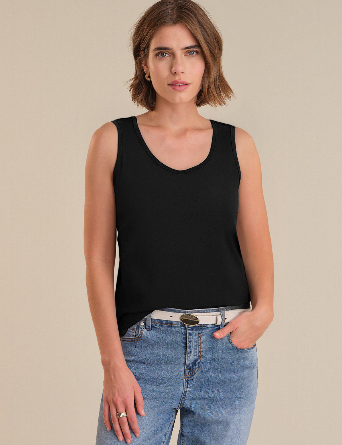 Woman wearing a black tank top and blue jeans on a beige background