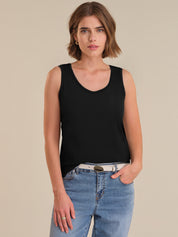 Woman wearing a black tank top and blue jeans on a beige background