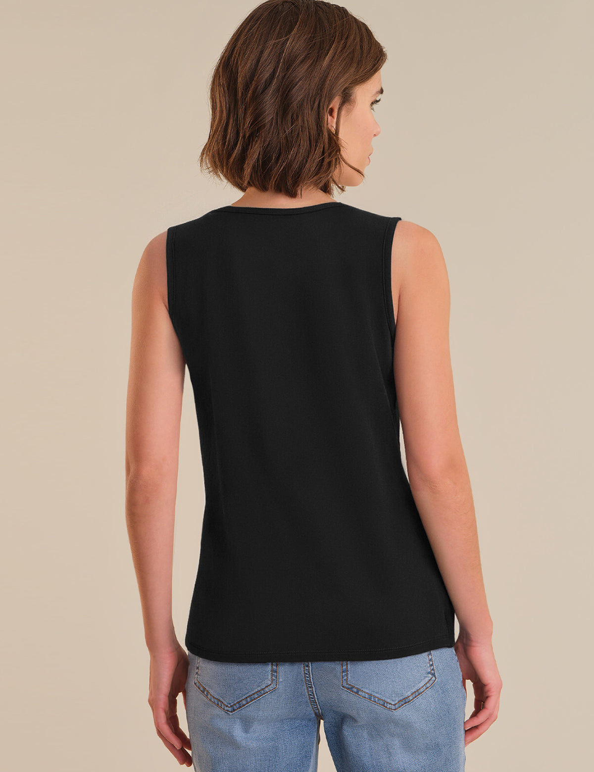 Person wearing a black sleeveless top and blue jeans on a beige background