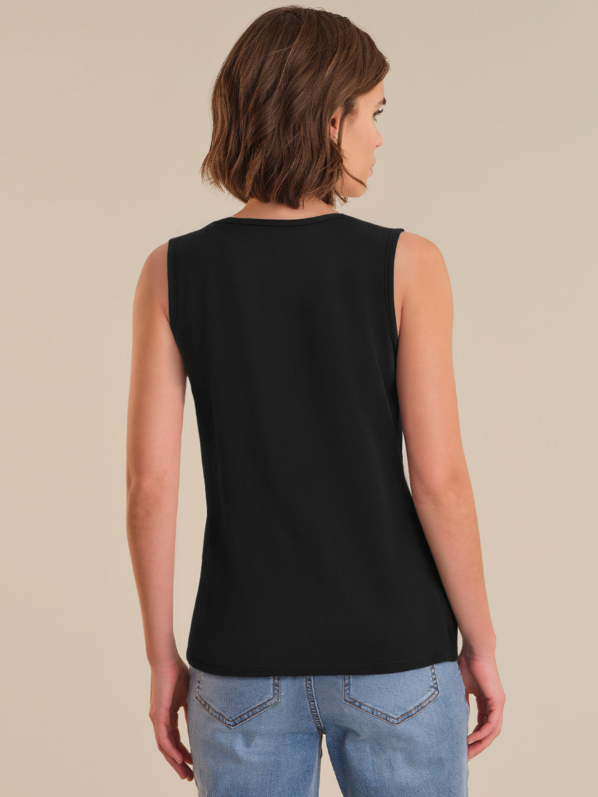 Person wearing a black sleeveless top and blue jeans on a beige background