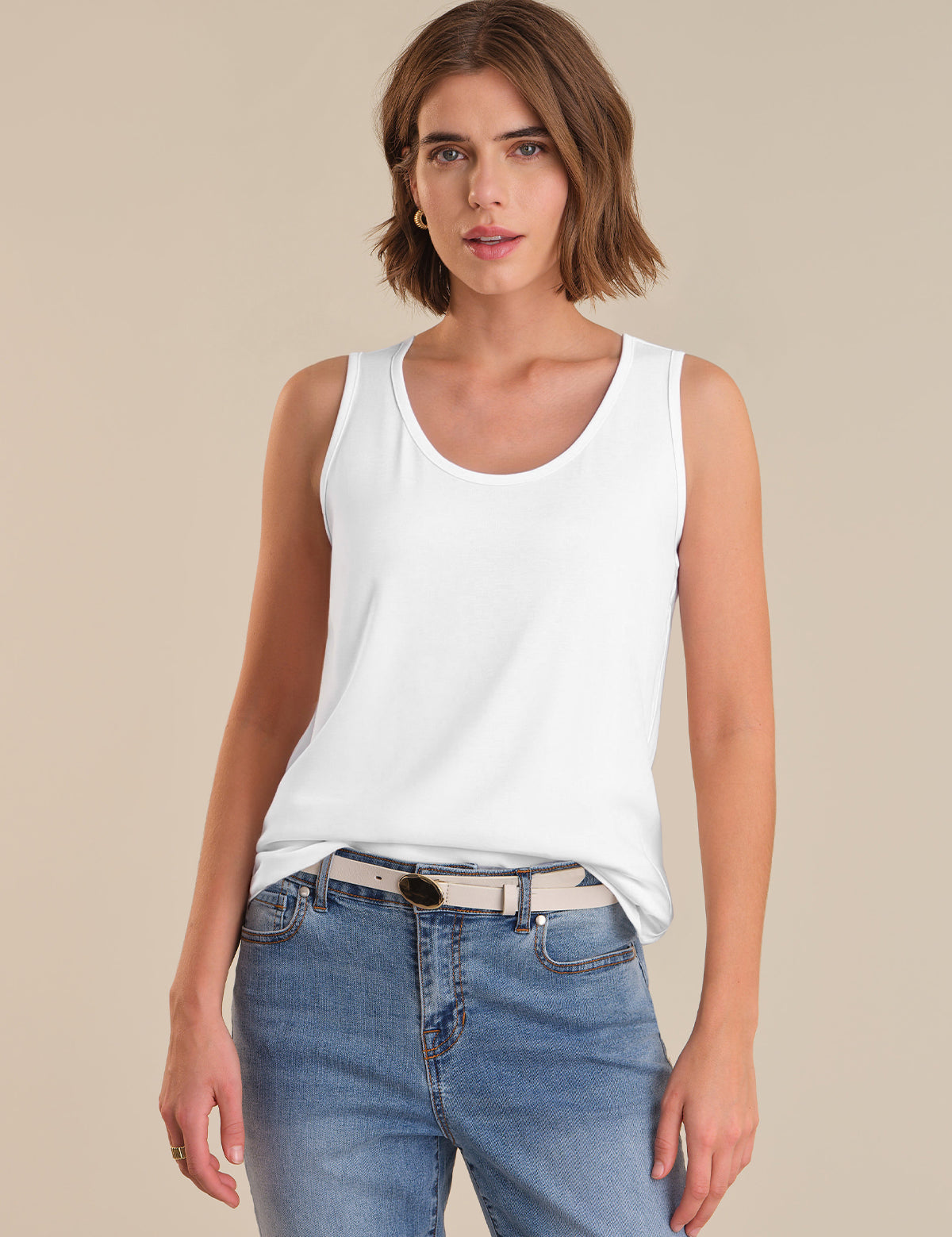 Woman wearing a white tank top and blue jeans against a beige background