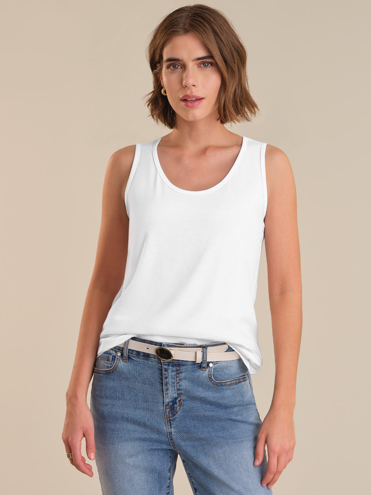 Woman wearing a white tank top and blue jeans against a beige background