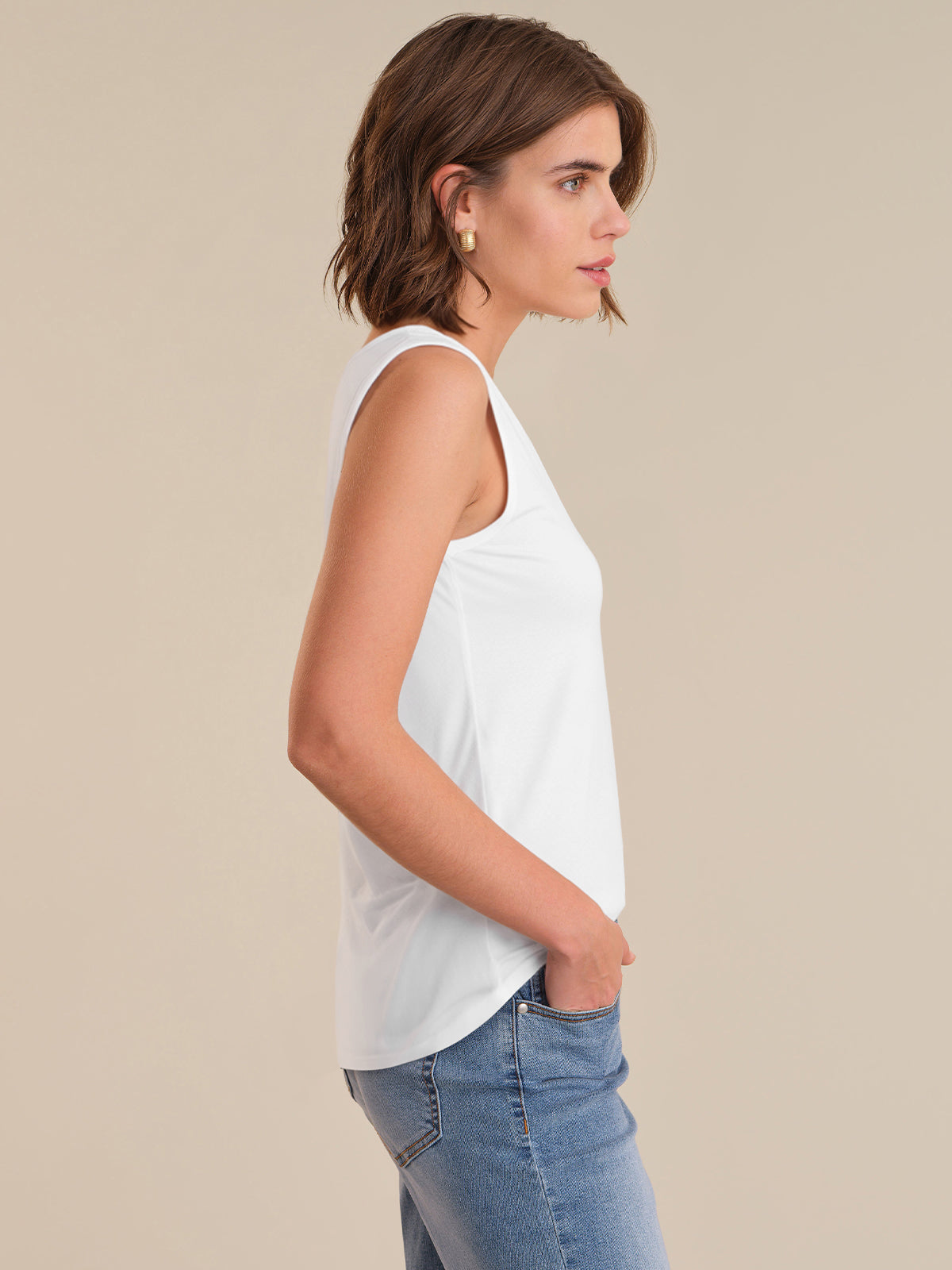 Woman wearing a white sleeveless top and blue jeans on a beige background