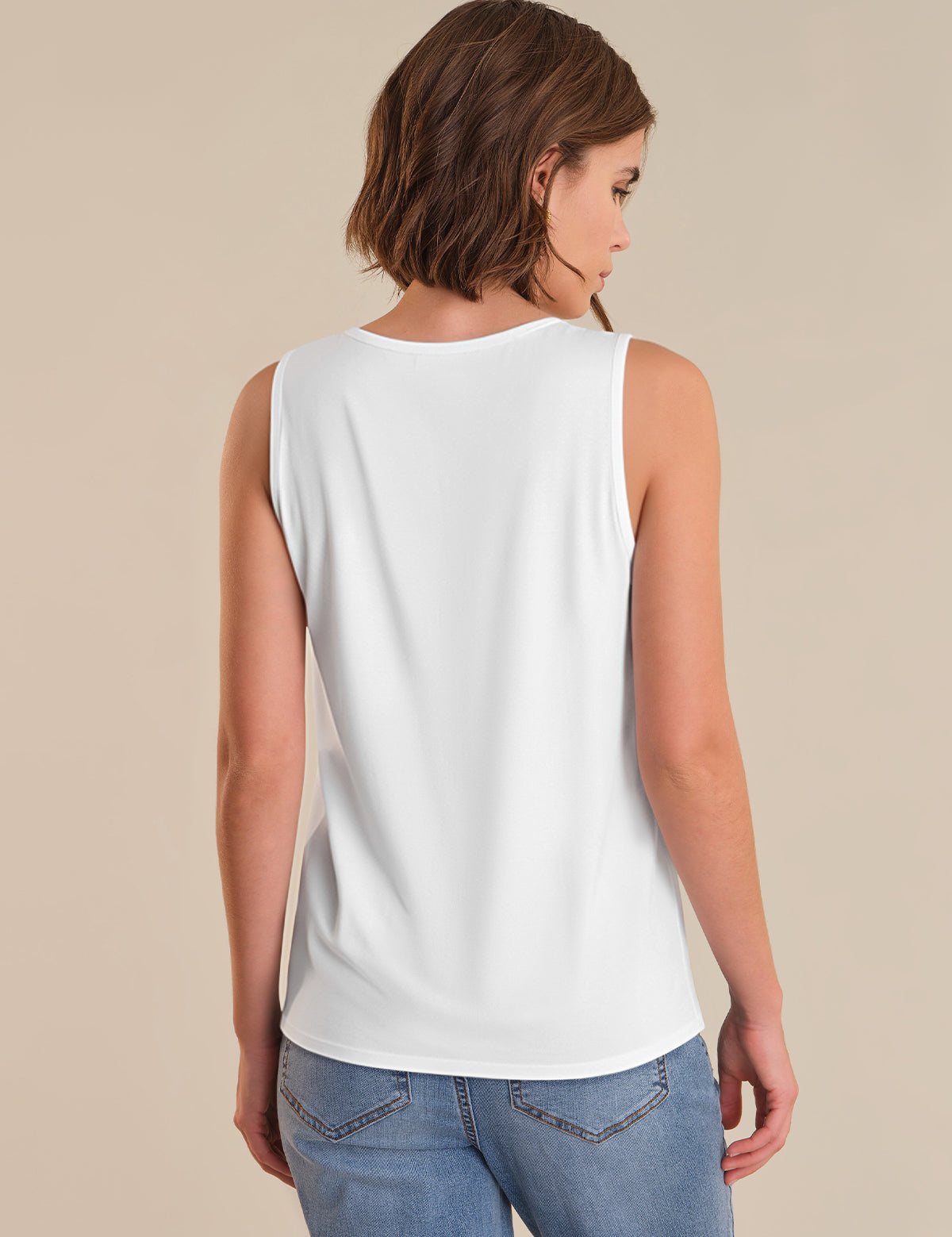 Woman wearing a white sleeveless top and blue jeans on a beige background