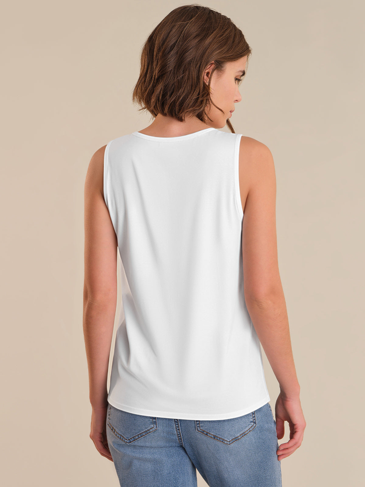 Woman wearing a white sleeveless top and blue jeans on a beige background