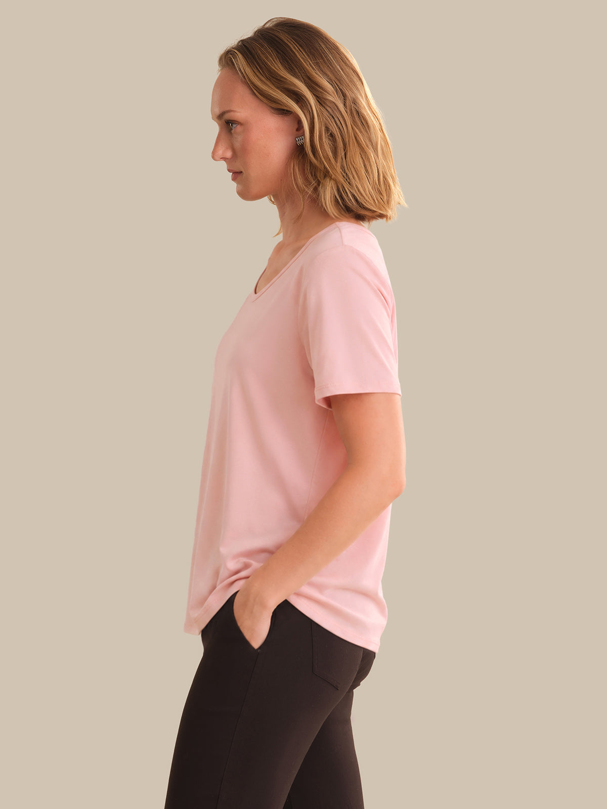 Woman wearing a pink t-shirt and black pants against a beige background
