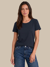 A woman modeling a dark navy blue short-sleeve crewneck t-shirt paired with blue jeans, set against a solid beige background.