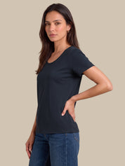 A woman modeling a dark navy blue short-sleeve scoop neck t-shirt paired with blue jeans, set against a solid beige studio background.