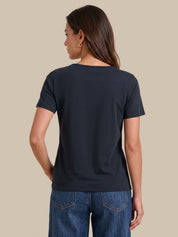 A woman shown from the back wearing a dark navy blue short-sleeve crewneck t-shirt and blue jeans, set against a solid beige background.