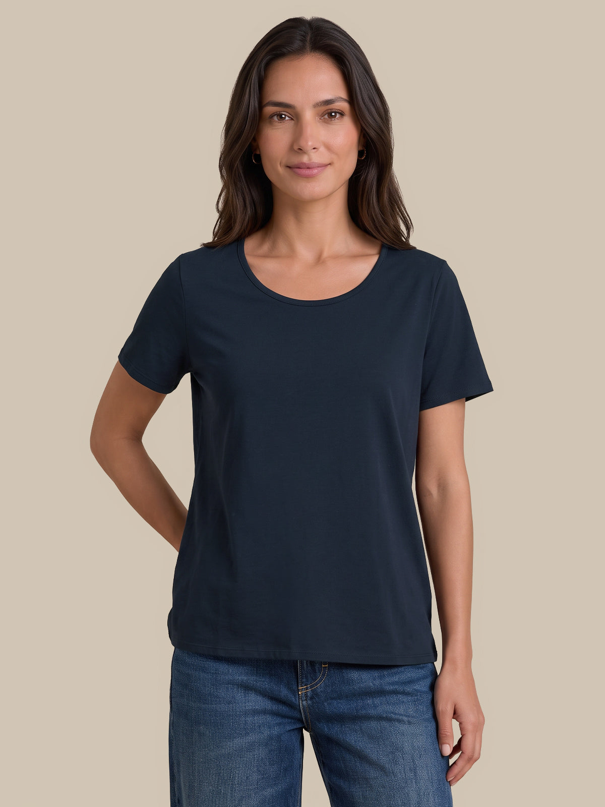 A woman modeling a dark navy blue short-sleeve crewneck t-shirt with blue jeans, standing against a solid beige background.
