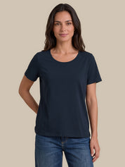 A woman modeling a dark navy blue short-sleeve crewneck t-shirt with blue jeans, standing against a solid beige background.