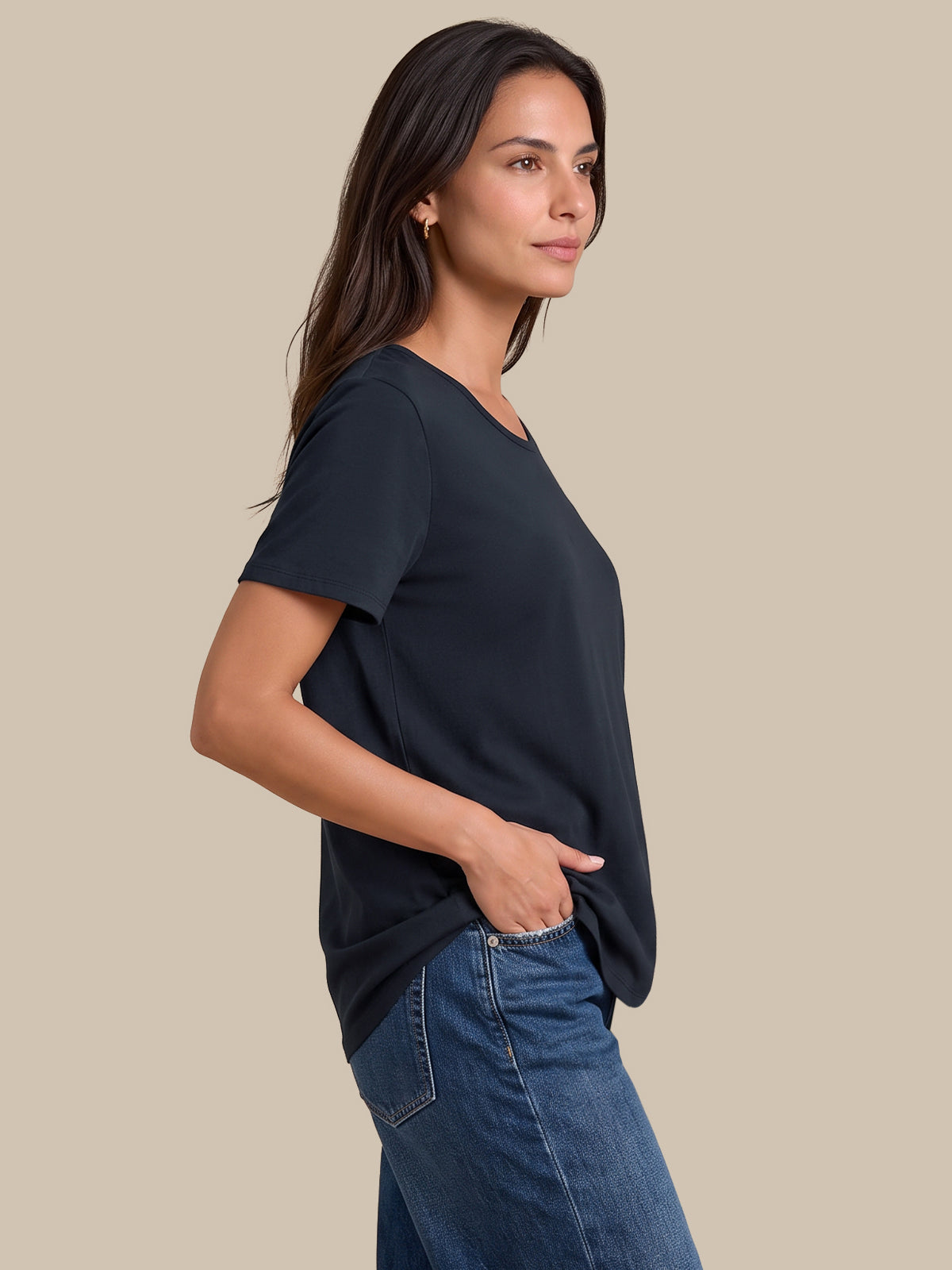 A woman wearing a dark navy blue short-sleeve top and blue jeans, shown from a side profile against a solid beige background.