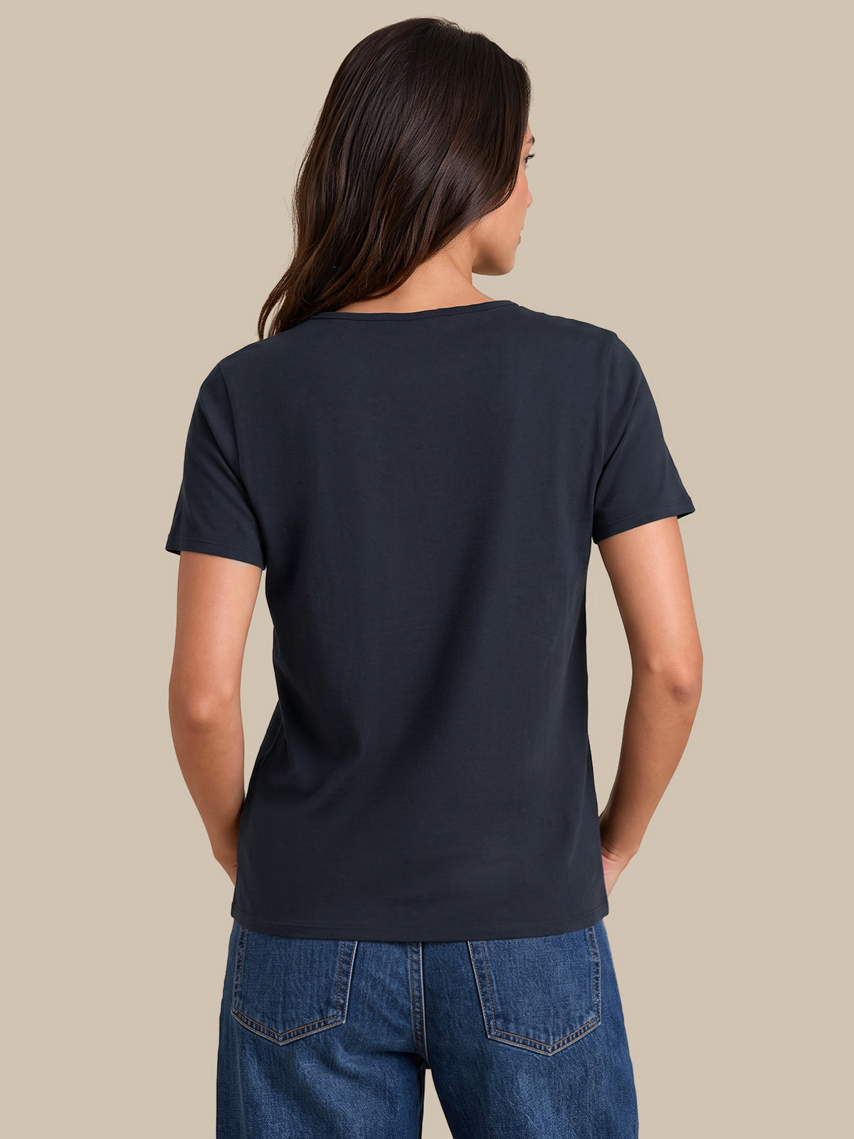 A woman viewed from the back wearing a dark navy blue short-sleeve crewneck t-shirt and blue jeans, set against a solid beige background.