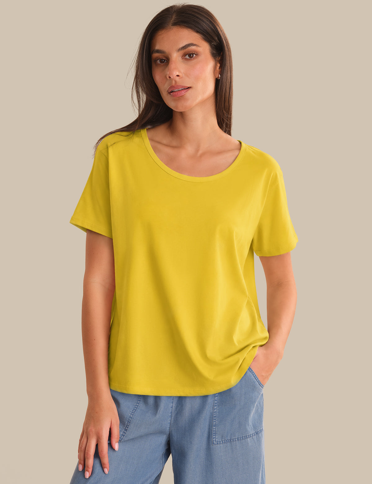Woman wearing a yellow t-shirt and blue jeans against a beige background