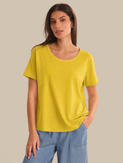 Woman wearing a yellow t-shirt and blue jeans against a beige background