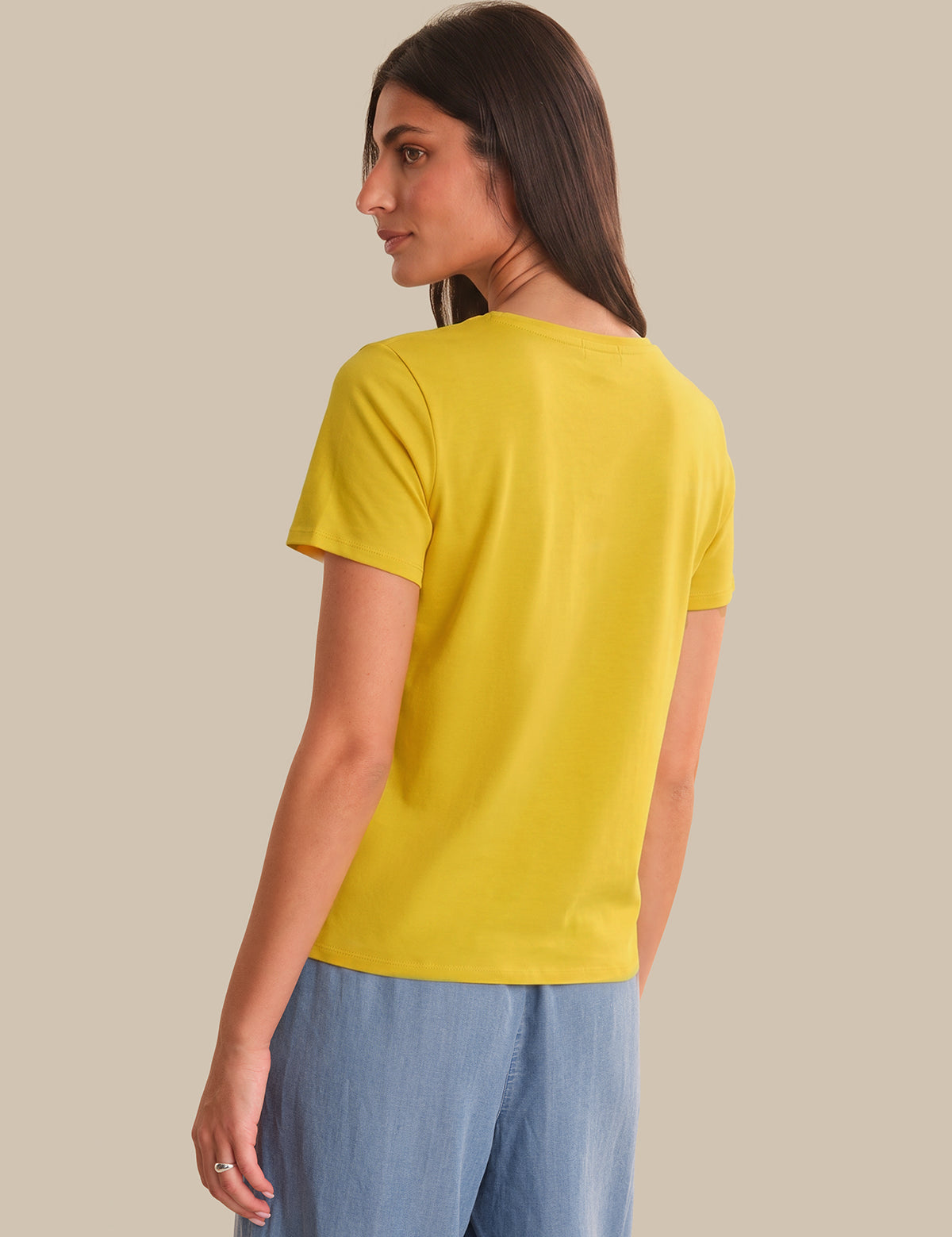 Woman wearing a yellow t-shirt and blue pants on a beige background