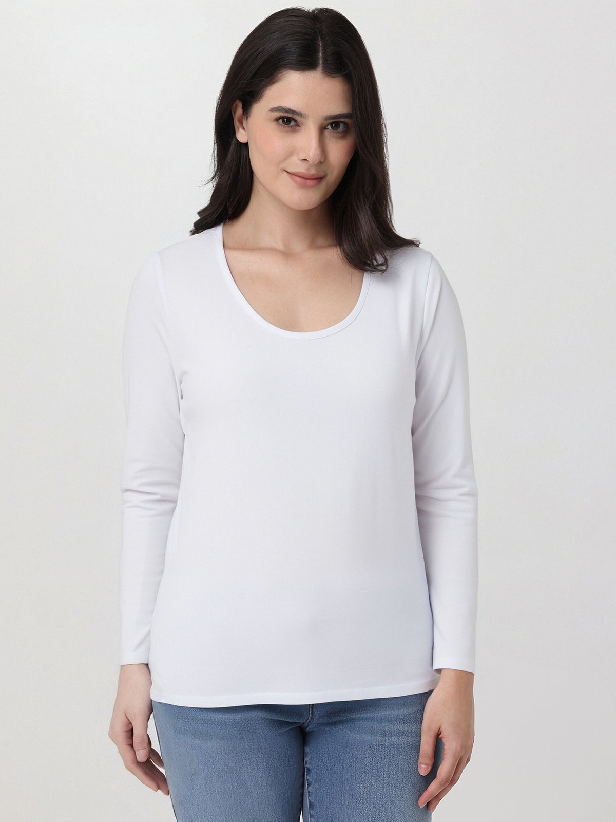 Woman wearing a white long-sleeve top and blue jeans on a plain background