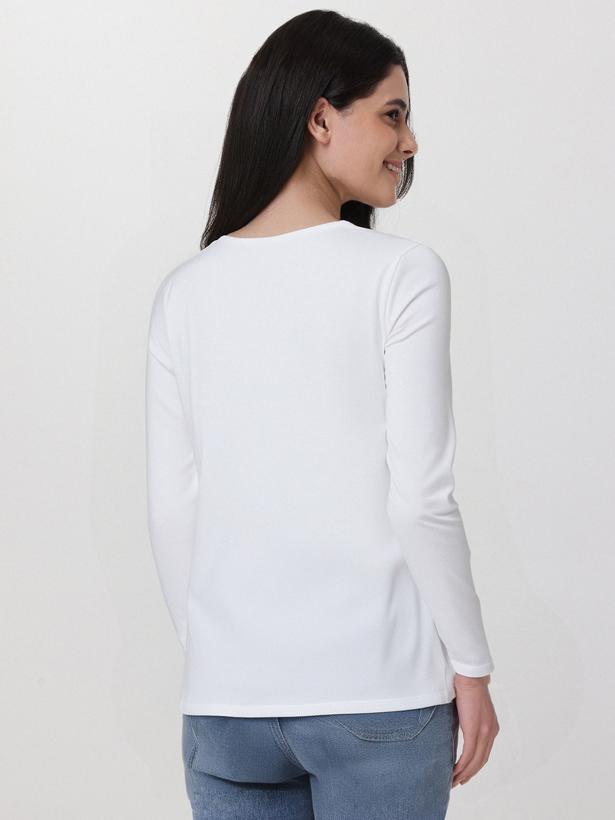 Woman wearing a white long-sleeve top and blue jeans on a plain background