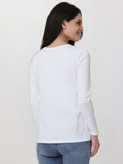 Woman wearing a white long-sleeve top and blue jeans on a plain background