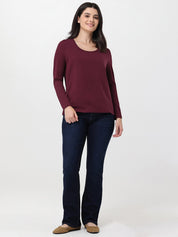 Woman wearing a burgundy long-sleeve top and dark blue jeans on a white background