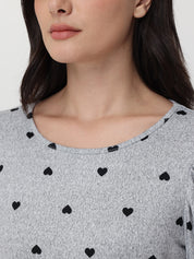 Close-up of a person wearing a gray top with black heart patterns on a plain background