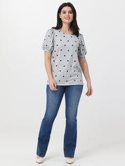 Woman wearing a gray blouse with black heart patterns and blue jeans on a white background