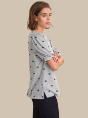 Woman wearing a gray blouse with black patterns on a beige background