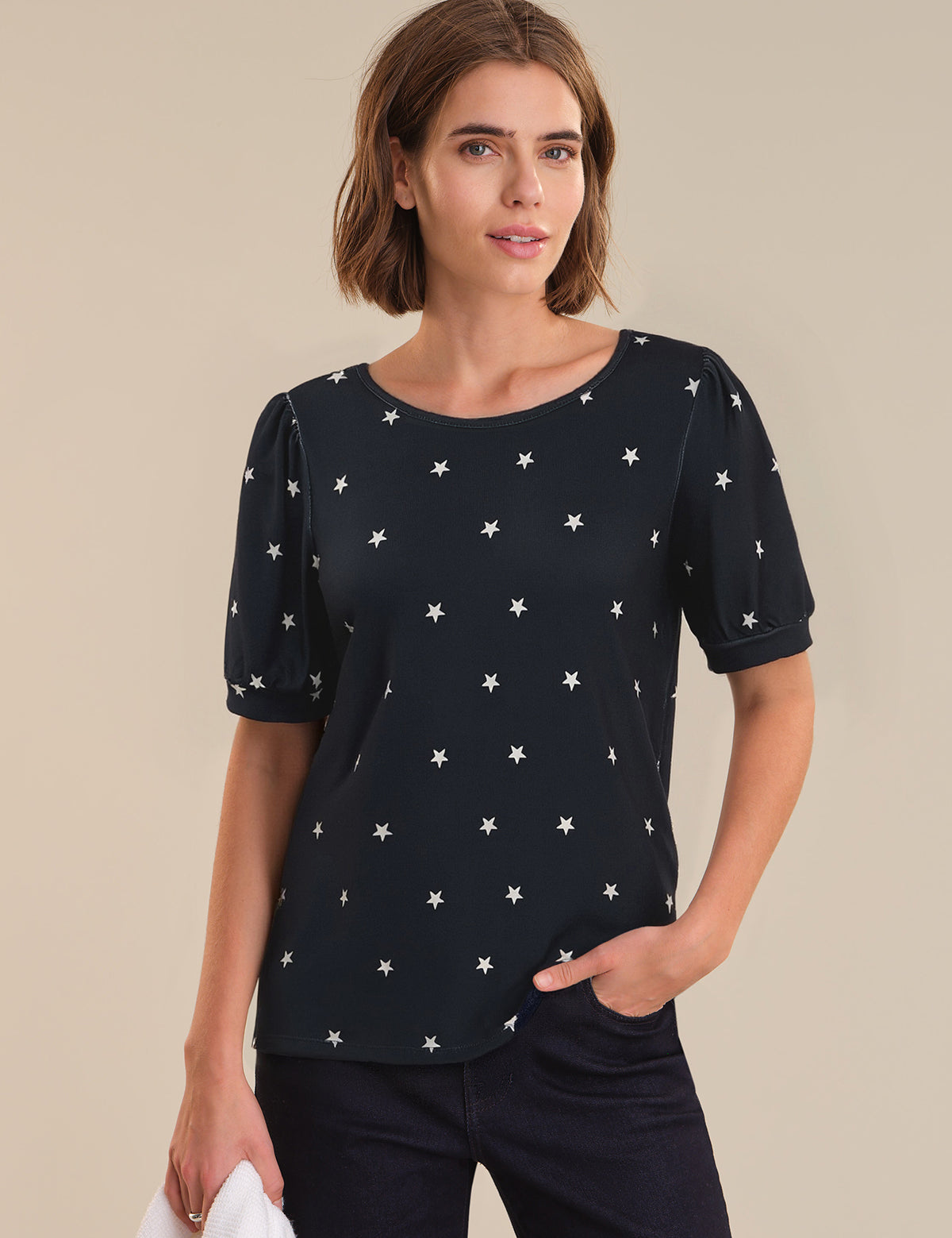Woman wearing a navy top with star pattern against a beige background