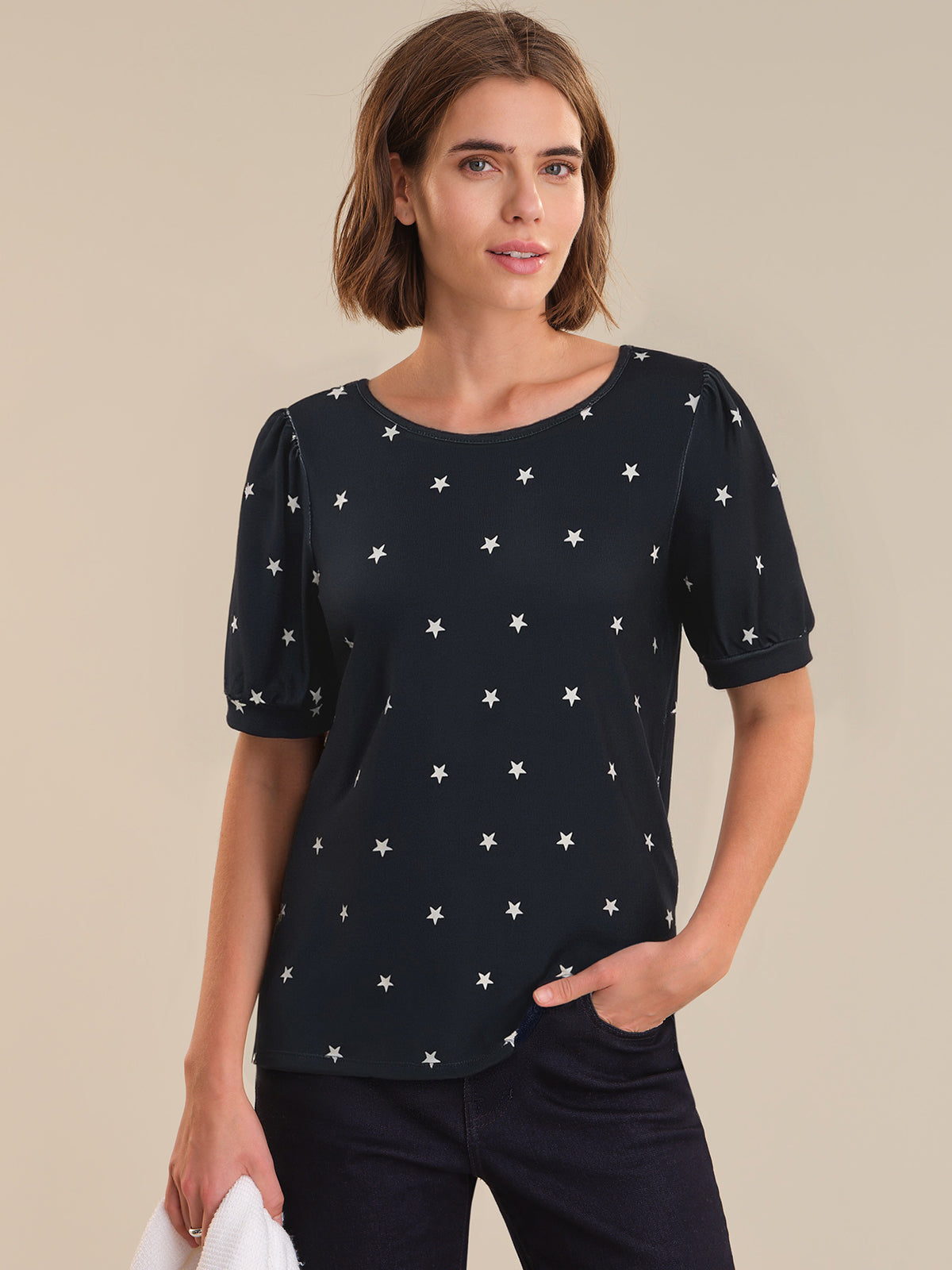 Woman wearing a navy top with star pattern against a beige background