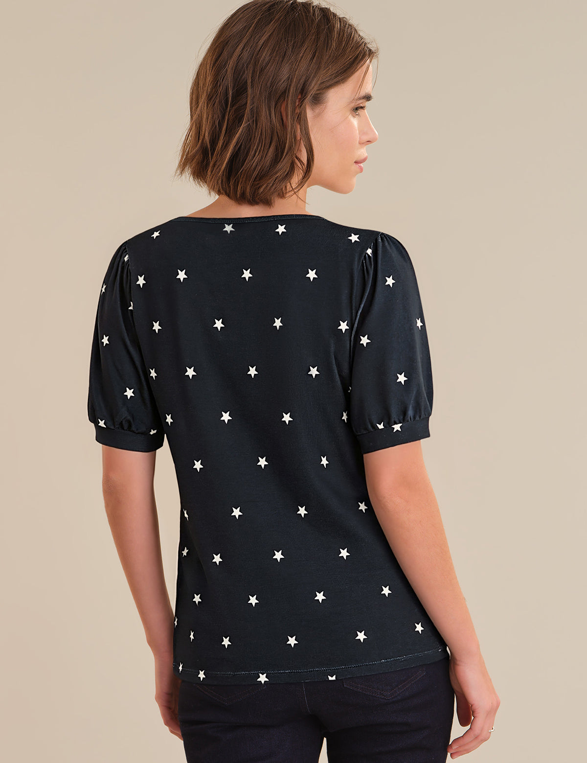 Woman wearing a navy top with white star pattern on a beige background