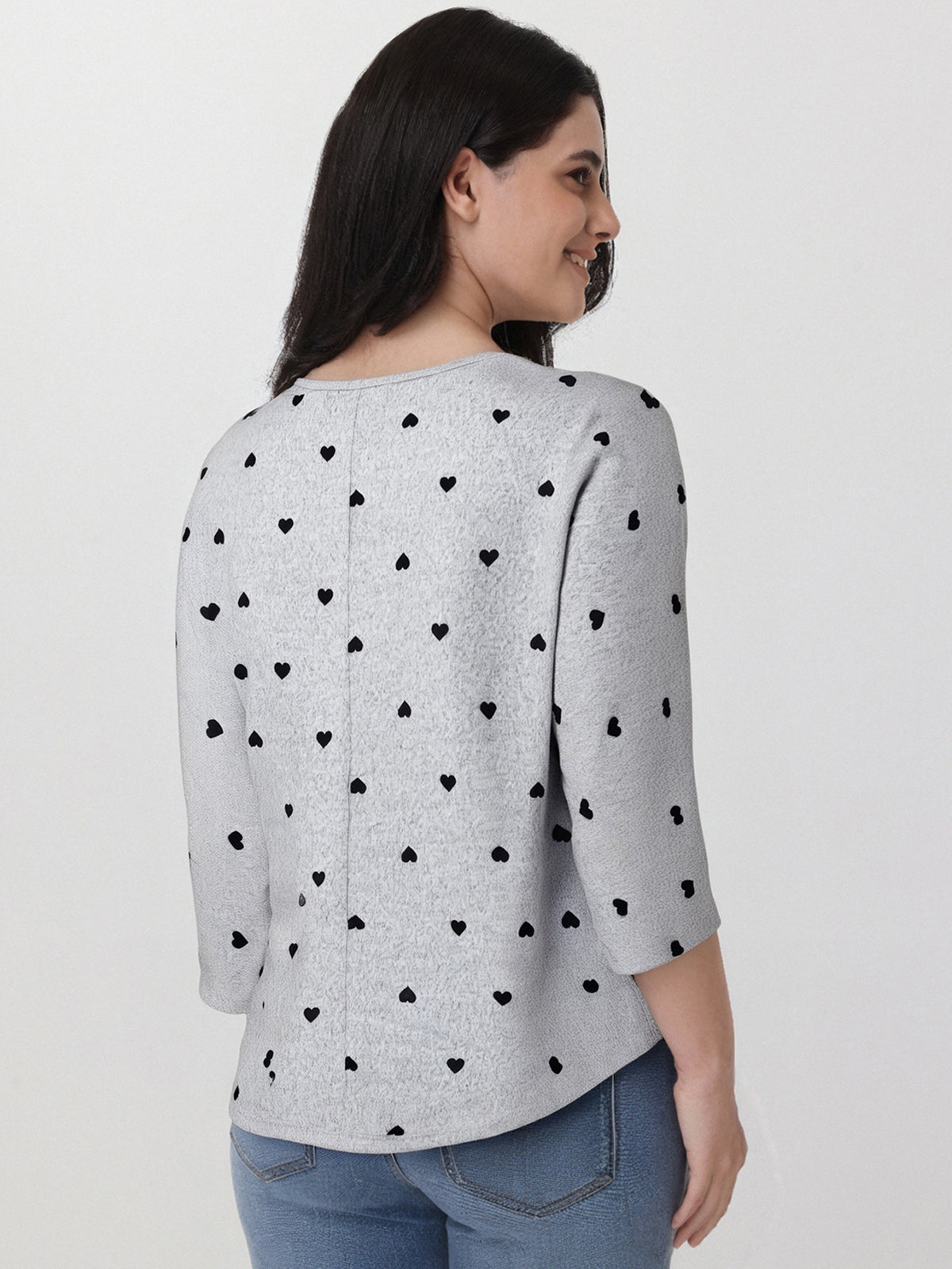 Woman wearing a gray sweater with black heart patterns on a plain background