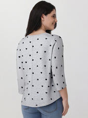 Woman wearing a gray sweater with black heart patterns on a plain background