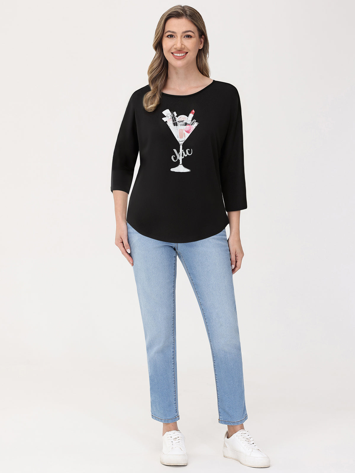 Woman wearing a black top with a graphic design and light blue jeans on a white background