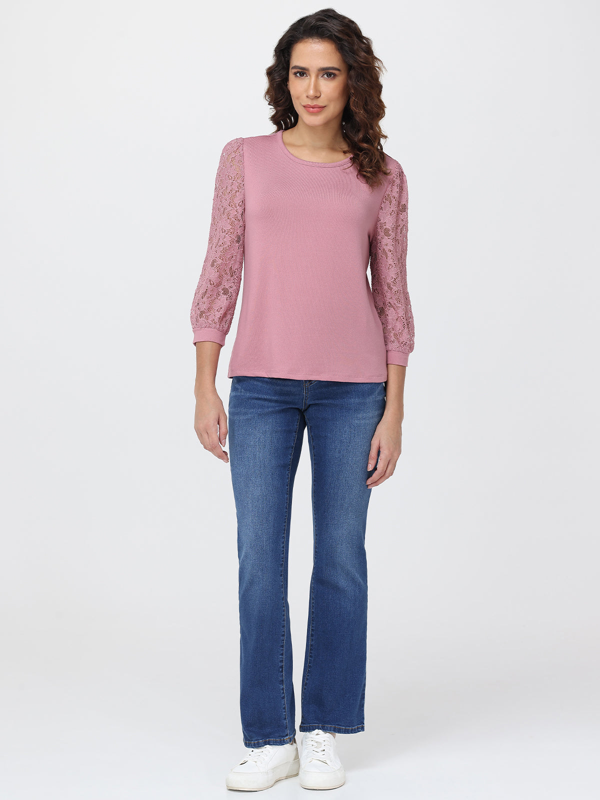 Woman wearing a pink blouse with lace sleeves and blue jeans on a white background