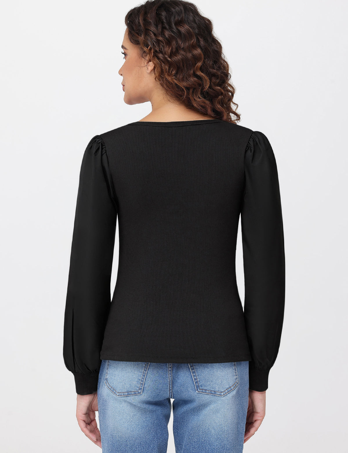 Woman wearing a black long-sleeve top and blue jeans on a light gray background