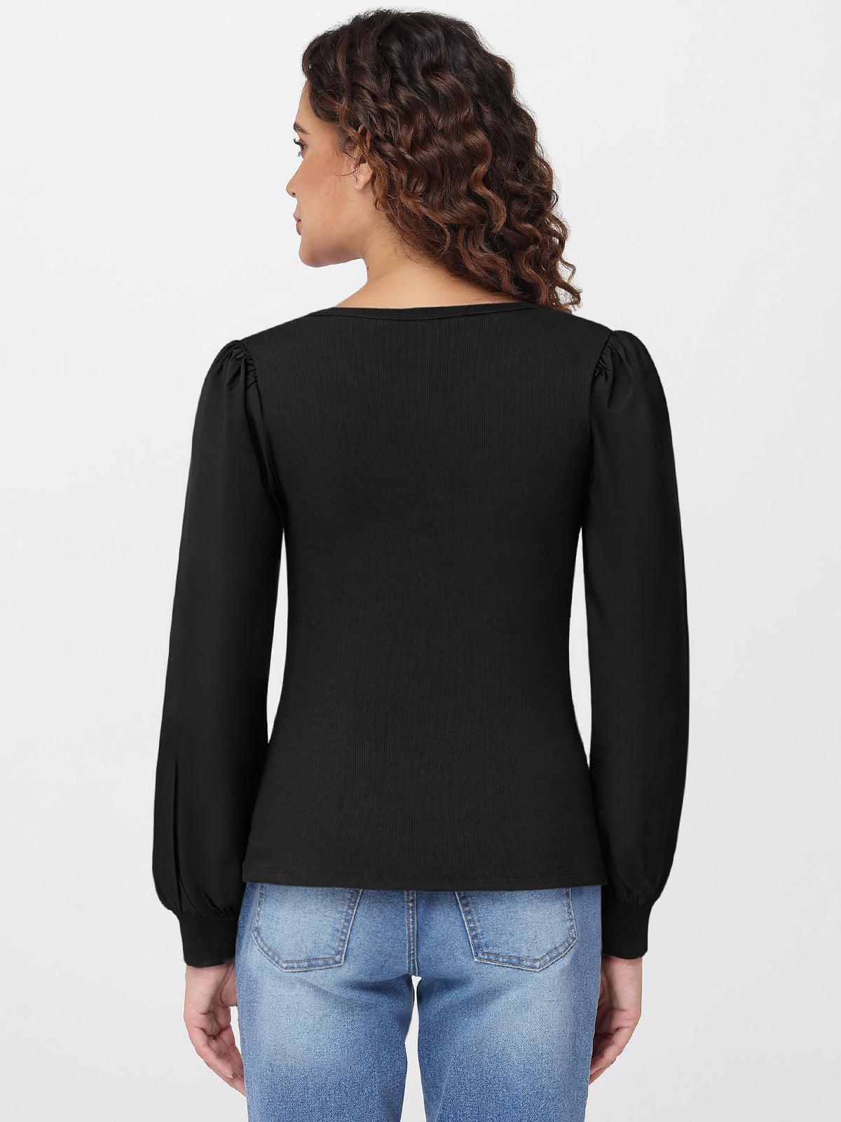 Woman wearing a black long-sleeve top and blue jeans on a light gray background