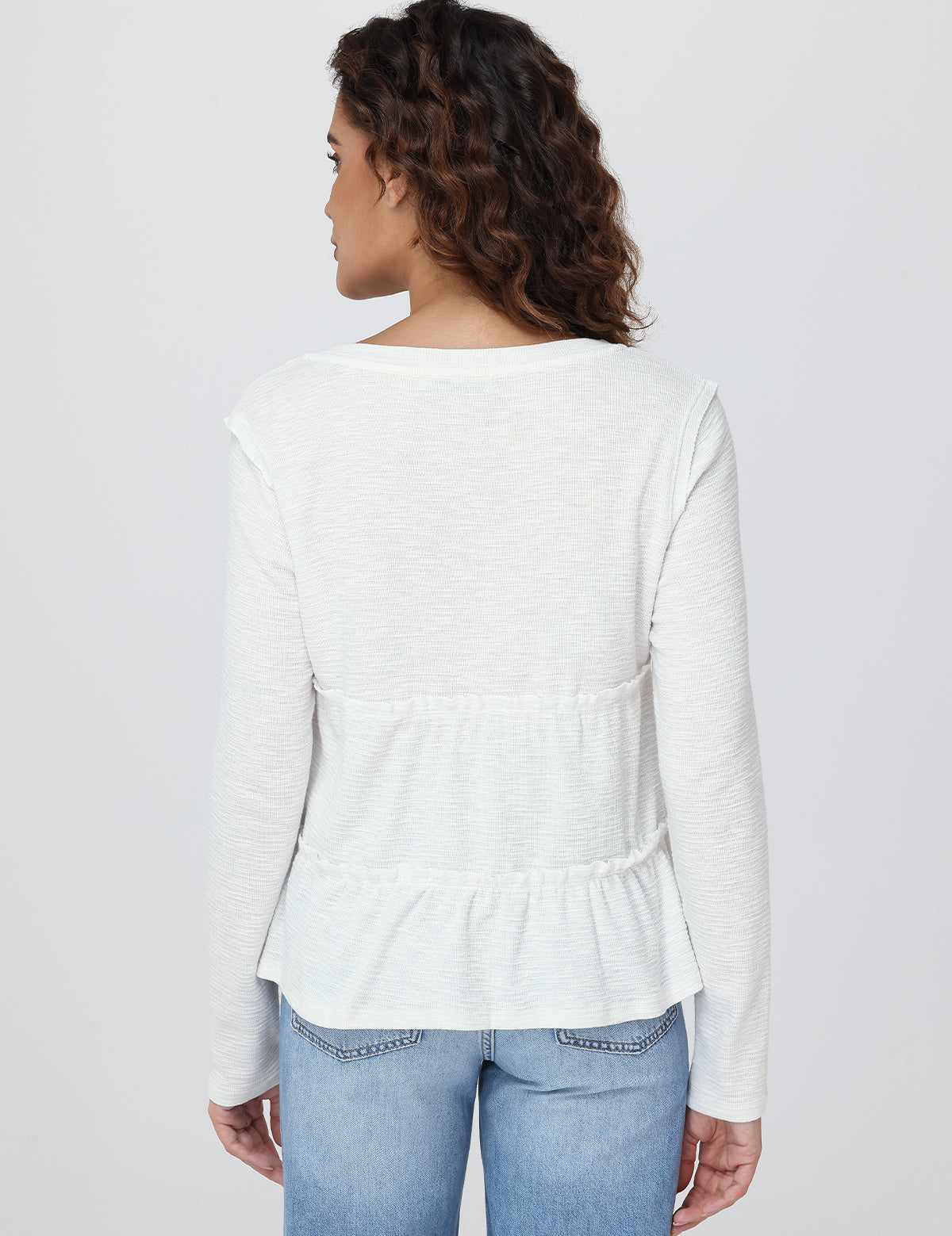 Woman wearing a white peplum top and blue jeans on a plain background