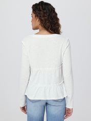 Woman wearing a white peplum top and blue jeans on a plain background