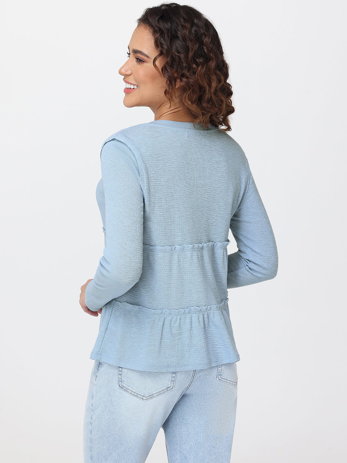 Woman wearing a light blue peplum top and jeans on a white background