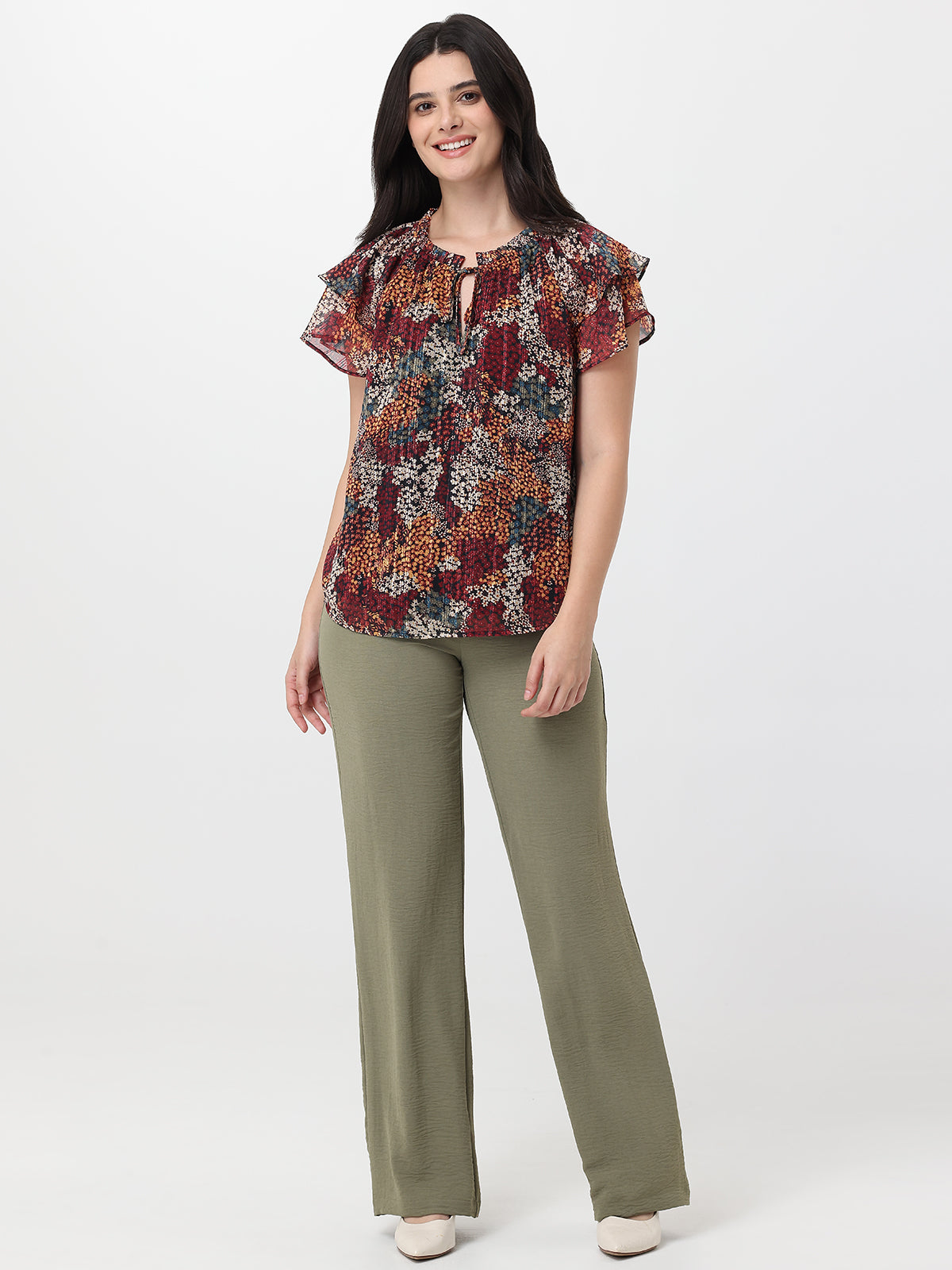 Woman wearing a patterned top and green pants on a white background