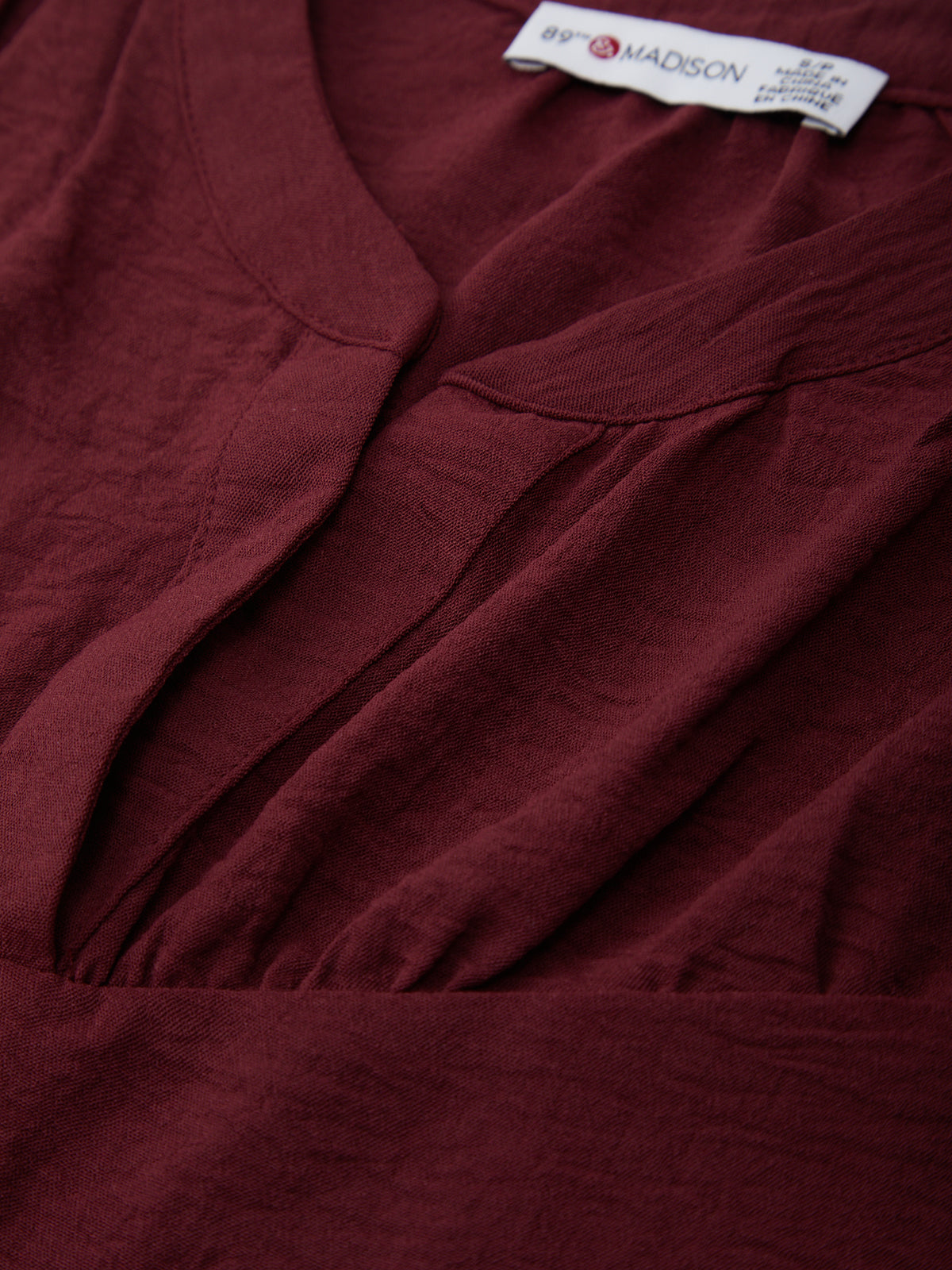 Close-up of a burgundy garment with a brand label on a plain background