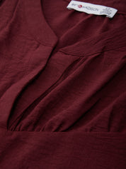 Close-up of a burgundy garment with a brand label on a plain background