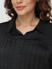Close-up of a person wearing a black pleated blouse against a neutral background
