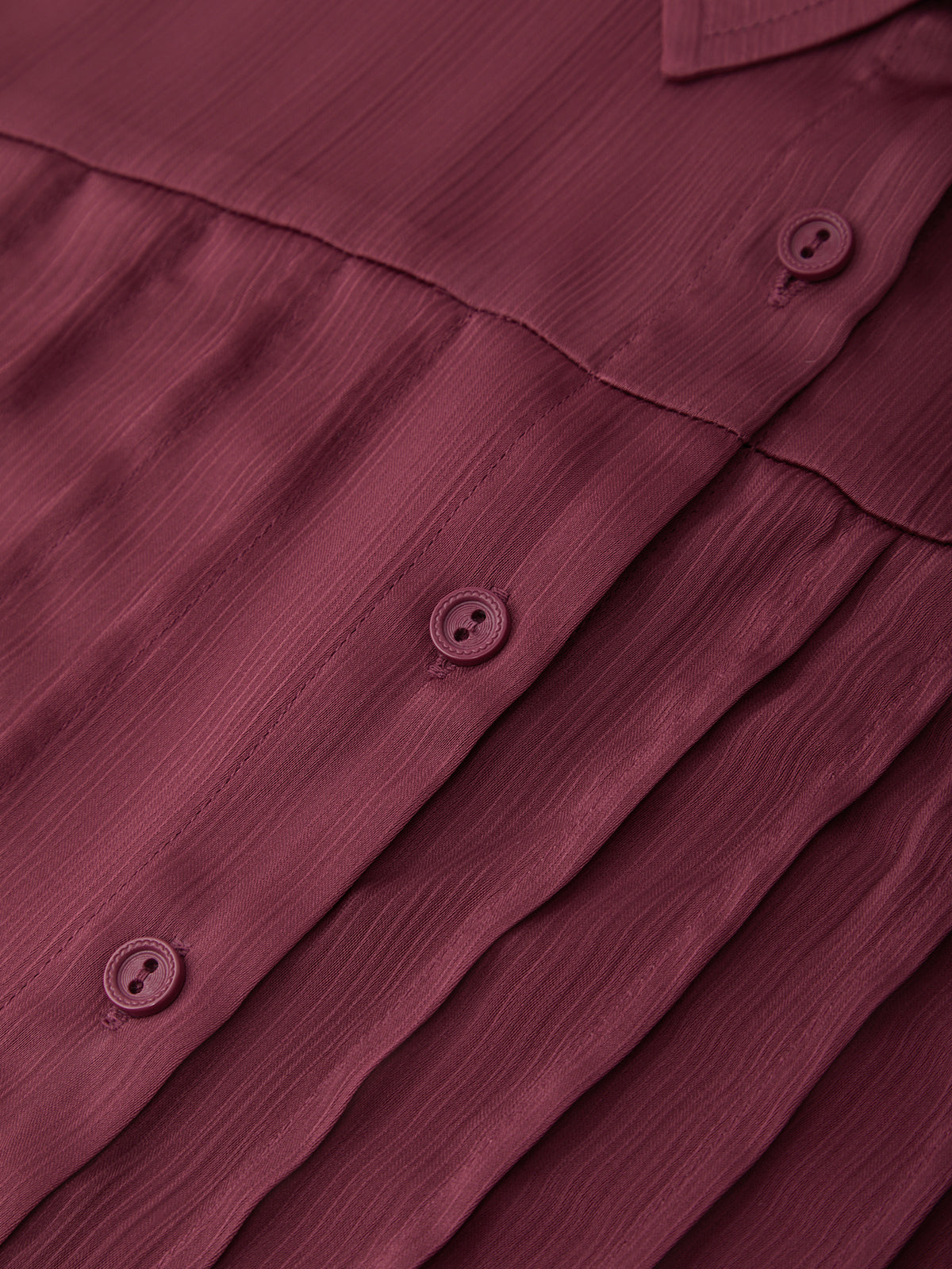 Close-up of a maroon shirt with buttons on a matching fabric background
