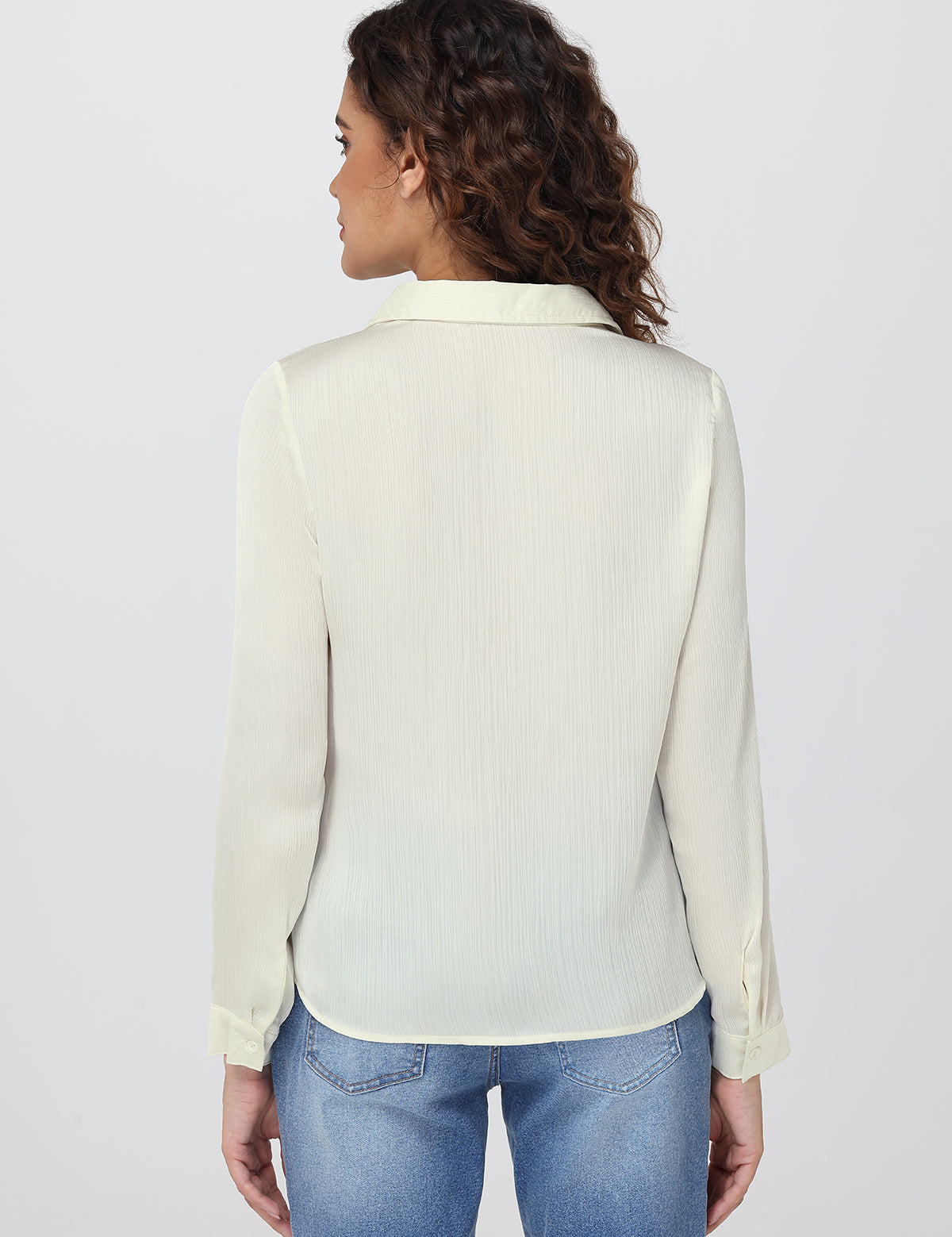 Woman wearing a light-colored blouse and blue jeans on a plain background