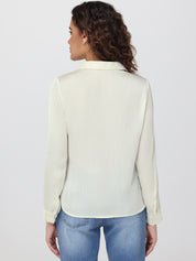 Woman wearing a light-colored blouse and blue jeans on a plain background