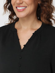 Close-up of a person wearing a black blouse with a plain background